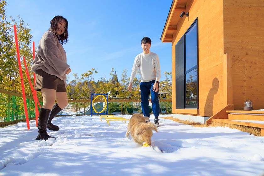 雪が積もったプライベートドッグランで遊ぶわんちゃんとカップル