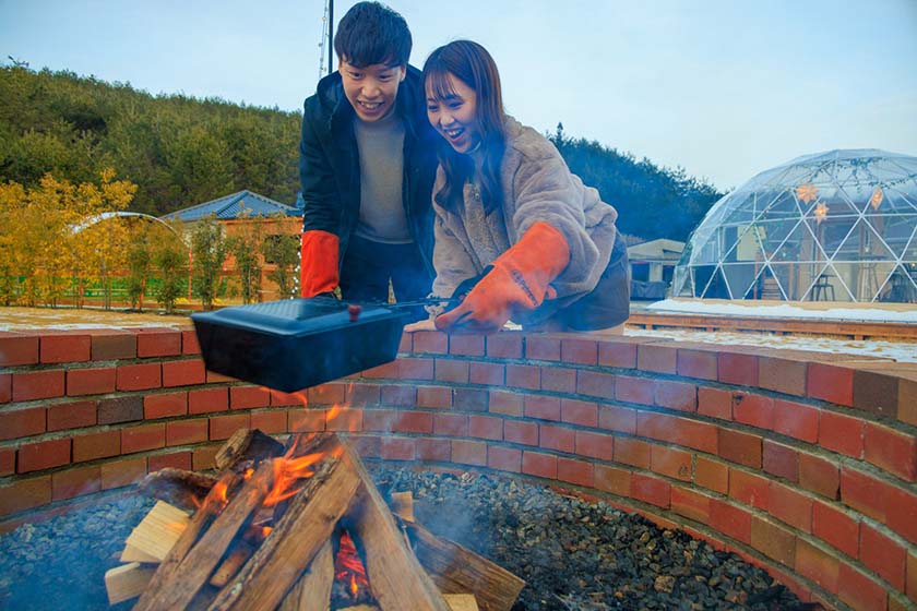 Two people enjoying making popcorn by a bonfire